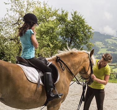 Reitlehrerin zäumt hellbraunes Pferd für Schülerin auf