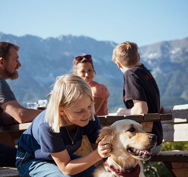 Mädchen sitzt auf Holzbank und streichelt Golden Retriever Hund