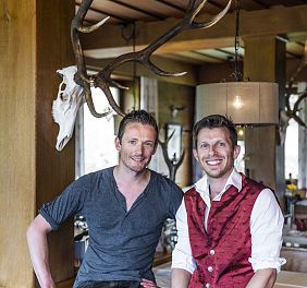 Zwei Männer sitzen auf Holzgeländer in einer Gaststube