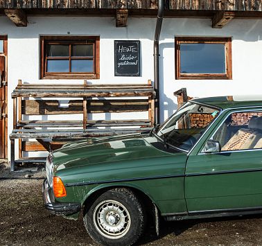 Grünes Auto der Marke Mercedes Parkt vor Bauernhof