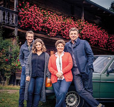 Vier Menschen stehen vor Auto und Haus mit Blumenschmuck