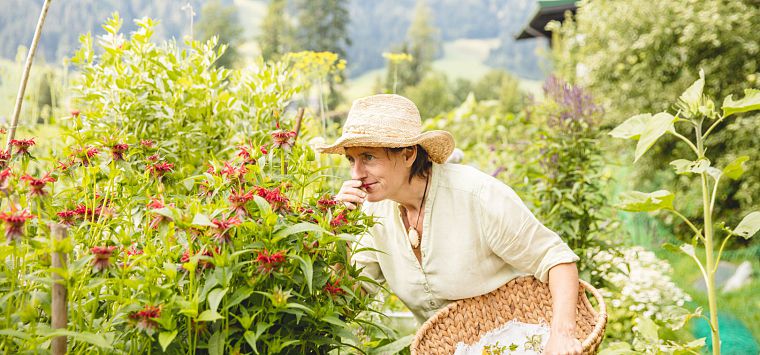 Frau mit Korb in einer Hand riecht an einer roten Blume