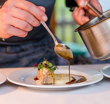 Mit Löffel wird eine brauen Sauce auf den Teller verteilt