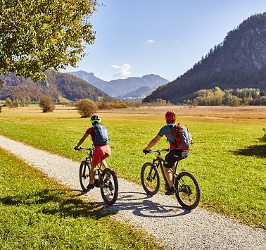 Zwei Radfahrer auf Radweg der durch grüne Wiesen führt