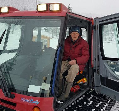 Mann in Winterbekleidung sitzt in Loipenwalze