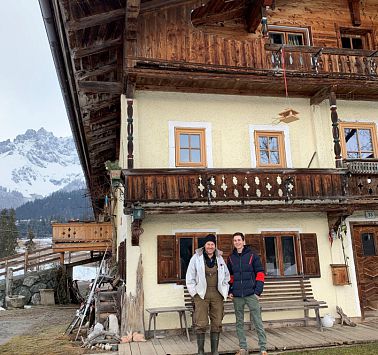 Zwei Männer stehen in Arbeitskleidung vor Bauernhof