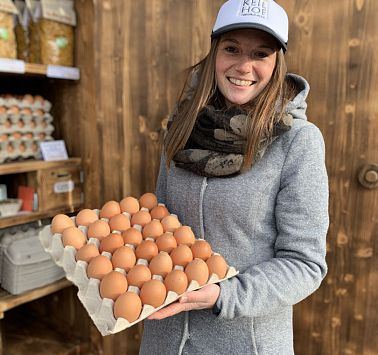 Junge Frau hält einen Karton voller Eier in der Hand