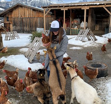 Junge Frau hält Huhn auf dem Arm und streichelt die Ziegen