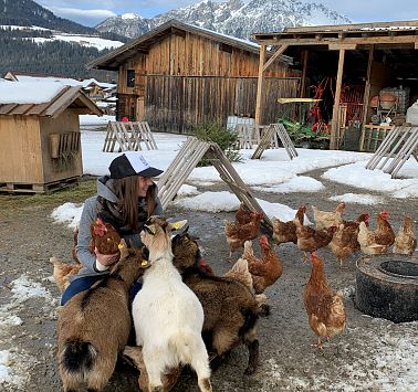 Frau kniet am Boden und streichelt die Ziegen