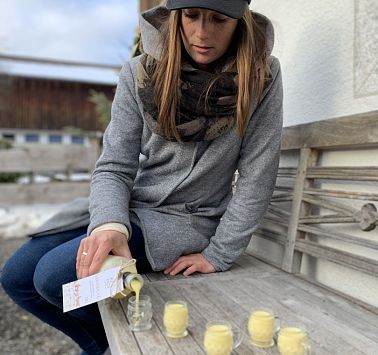 Frau sitzt auf Bank und schenkt Eierlikör in kleine Gläser