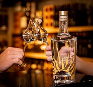 Zwei Hände stoßen mit Schnapsstamperl an