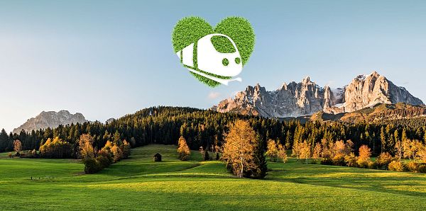 Herbstlandschaft in Tirol mit grünen Wiesen, farbenfrohen Bäumen und einem markanten Bergmassiv im Hintergrund. Ein Herz mit einem Zuglogo schwebt darüber.
