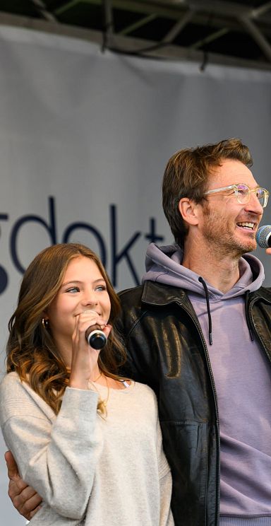 Two people on stage with microphones at a TV event. A banner in the background suggests a connection to the Wilder Kaiser region and its cultural offerings.