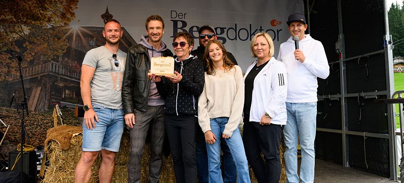 A group of people posing on a stage, some holding an award plaque. They are standing in front of a backdrop with the word "Bergdoktor."