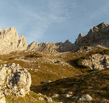 A golden-hued view of the Wilder Kaiser mountains with rocky peaks and gentle grassy slopes under the warm light of sunset, creating a picturesque alpine scene.