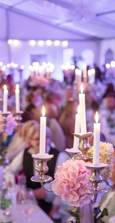 A large, elegant banquet with people seated at decorated tables, surrounded by lit candles and floral arrangements, creating a festive and formal atmosphere.