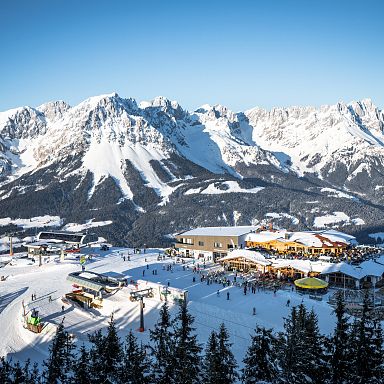 Snow-covered ski resort with chalets, surrounded by majestic mountain peaks under a clear blue sky, offering winter sports activities and scenic views.