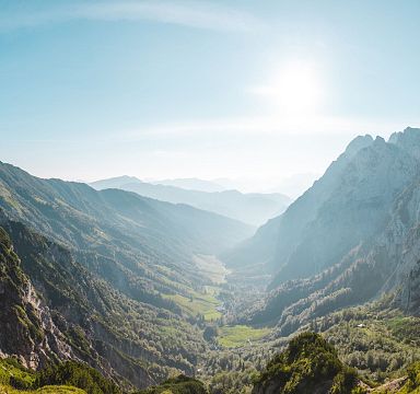 Atemberaubende Berglandschaft mit grünen Tälern und majestätischen Gipfeln unter blauem Himmel und strahlender Sonne.