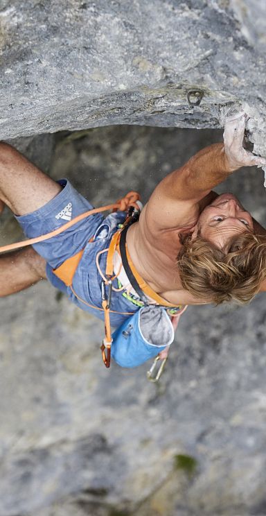 A rock climber in blue shorts ascends a steep, gray rock face, demonstrating strength and skill. The climber is secured with ropes and wears climbing gear.