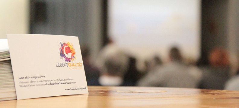 A focused business card with blurred figures in the background at a conference or meeting setting.