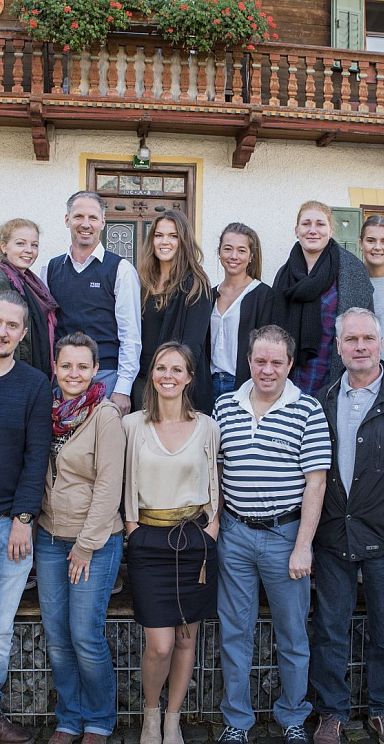 A group of people posing for a photo in front of a traditional alpine house with a wooden balcony and flowers.