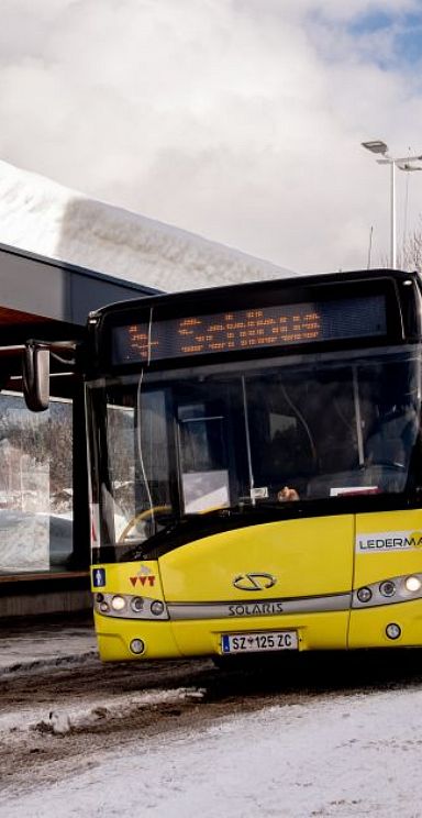 Zwei Skifahrerinnen an Haltestelle mit einfahrendem Bus