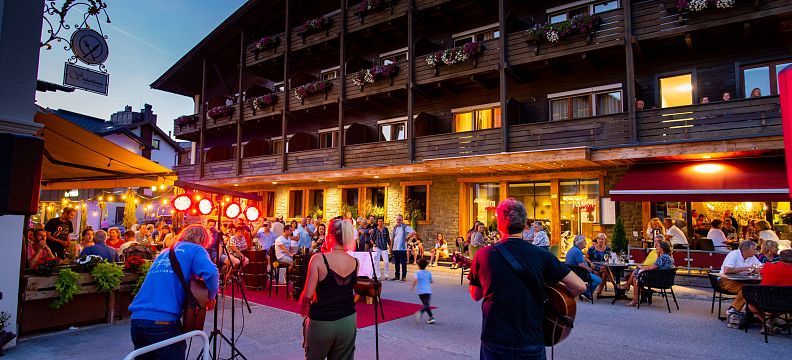 Musiker treten abends bei einem Open-Air-Konzert vor einem traditionellen Gebäude auf, während die Zuschauer in einer gemütlichen Umgebung sitzen und zuhören.