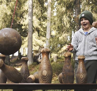A child and adult playing with wooden bowling pins in a forest in the Wilder Kaiser region, showcasing the fun and activities available in the area.