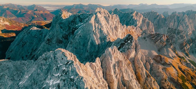 Luftaufnahme der beeindruckenden Felsen und Gipfel des Wilder Kaiser Massivs in Tirol, umgeben von malerischen Tälern unter einem klaren, blauen Himmel.