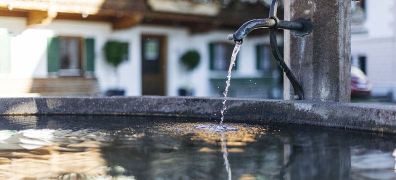 Close-up of a fountain with flowing water, set against a backdrop of traditional Tyrolean buildings adorned with flowers, in the Wilder Kaiser region.