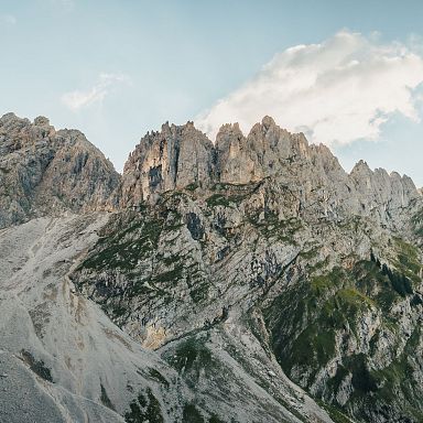 Majestätisches Bergmassiv mit zerklüfteten Felsen und steilen Hängen, teils von grüner Vegetation bedeckt, unter klarem Himmel mit wenigen Wolken.
