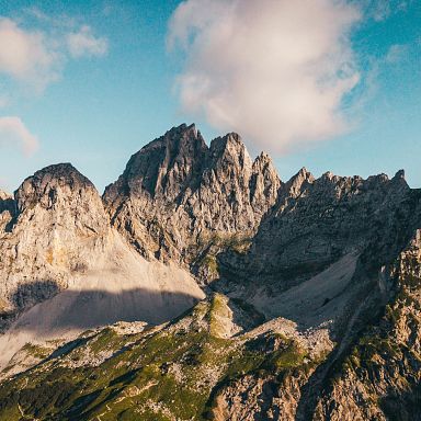 Imposante Berglandschaft mit schroffen Gipfeln unter blauem Himmel und vereinzelten Wolken. Die Sonne beleuchtet die felsigen Formationen der Tiroler Alpen.