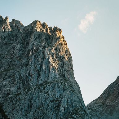 Steile Felsformationen des Wilden Kaisers heben sich gegen den blauen Himmel ab. Die Felsen sind von Sonnenlicht beleuchtet und zeigen deutliche Strukturen.