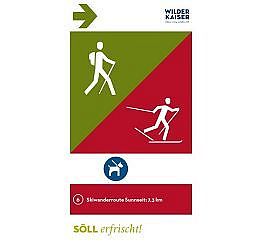 Sign showing hiking and skiing options at Wilder Kaiser in Söll, Austria. Green section indicates hiking, red for skiing, with a dog-friendly note below.