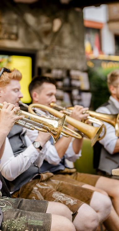 Tyrolean brass band in traditional attire performs outdoors at Wilder Kaiser, capturing cultural charm with instruments like trumpets and tubas in a scenic setting.