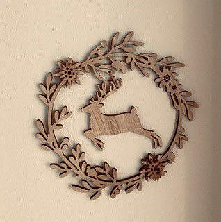 Ein hölzernes Ornament in Form eines springenden Hirsches, umgeben von floralen Mustern, hängt an einer Wand. Es vermittelt einen rustikalen, natürlichen Charme.
