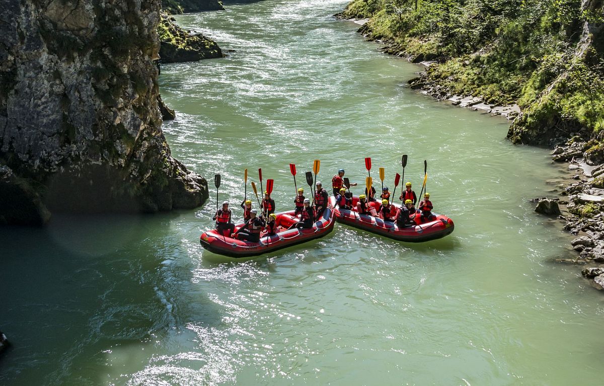 Groups of people rafting on a river in a lush, green forest within the Wilder Kaiser region, Austria, known for outdoor activities and scenic landscapes.