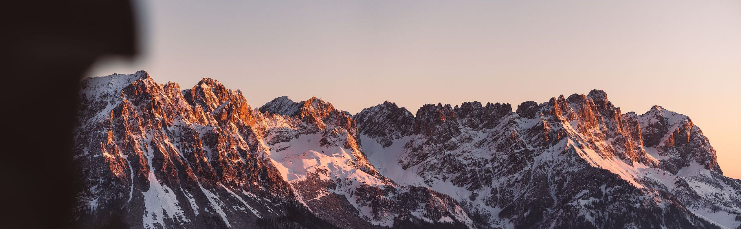 Majestätisches Bergpanorama bei Sonnenaufgang, schneebedeckte Gipfel leuchten im warmen Licht. Klare, ruhige Atmosphäre in den Alpen.