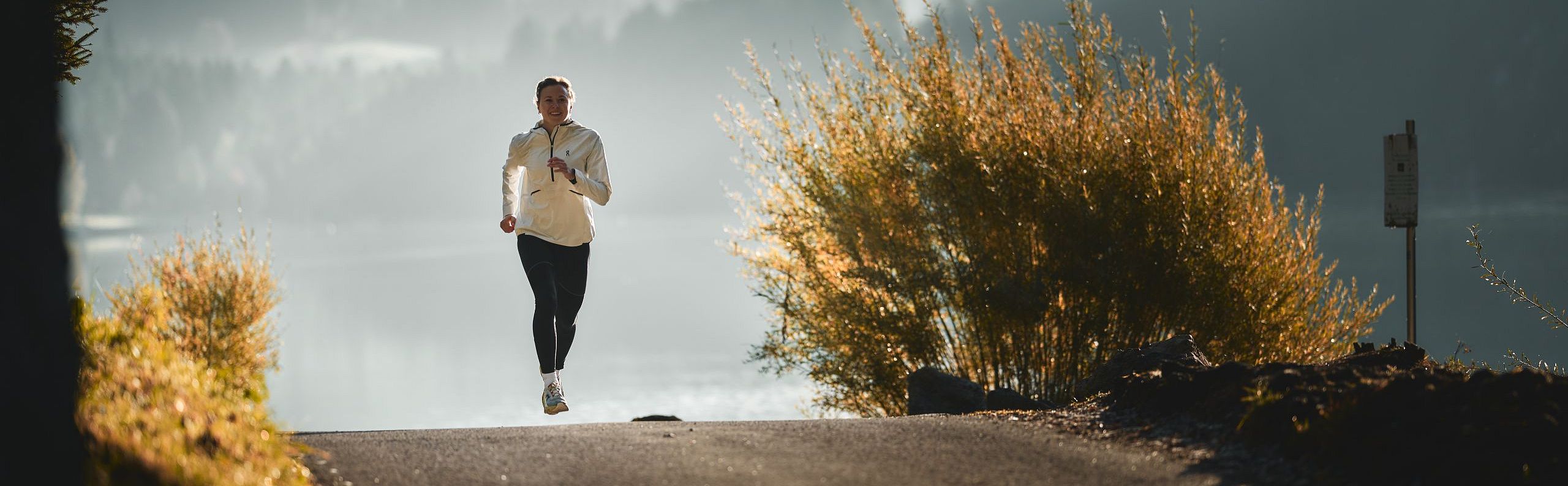 A man running on a forested path with mountains in the background, depicting the tranquil beauty of the Wilder Kaiser region.