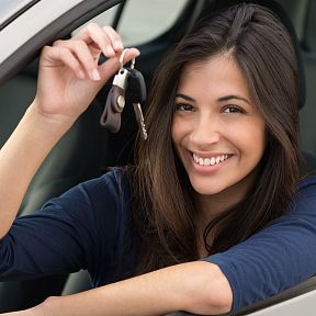 Person holding car keys, smiling inside a car with an open window.