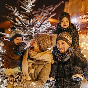 Happy family enjoying a winter evening, surrounded by snow and festive lights, standing near a decorated Christmas tree.