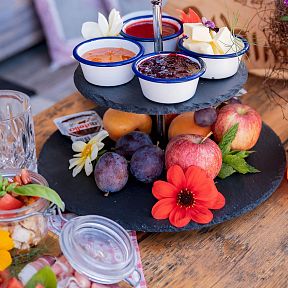 A breakfast spread featuring fruits, jams, and a drink on a table with colorful flowers, evoking a traditional Tyrolean setting under the majestic Wilder Kaiser.