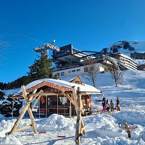 Snowy mountain scene at Wilder Kaiser with ski lift, cozy hut, and people enjoying winter activities. The peaks are covered in snow, creating a winter wonderland.