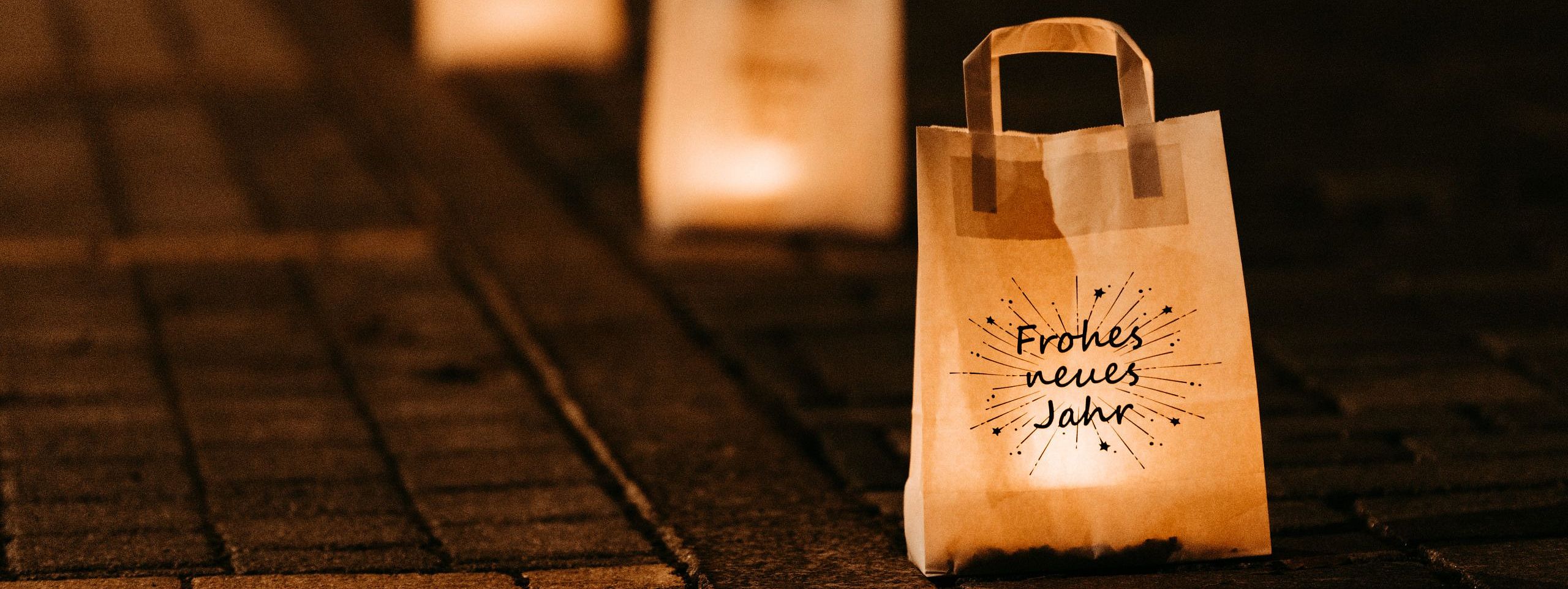 Leuchtende Papierlaternen in einer Reihe auf einer gepflasterten Straße, eine mit der Aufschrift "Frohes neues Jahr" im Vordergrund.