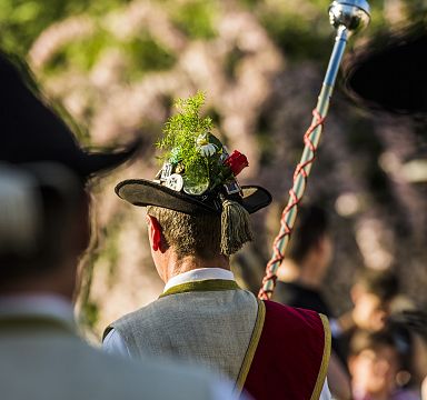 Menschen genießen ein Fest im Freien mit Bergen im Hintergrund. Es gibt Tische, Bäume und eine Kirche in der Nähe, unter strahlend blauem Himmel.