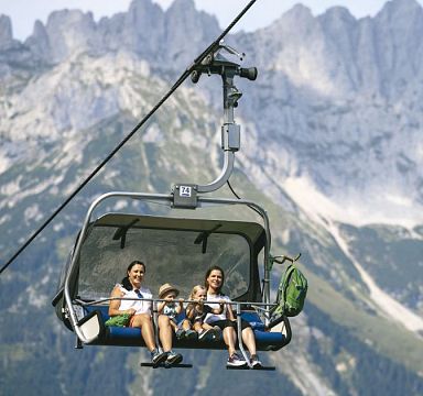 Zwei Freundinnen mit Kindern auf Sessellift vor Kulisse des Wilden Kaisers