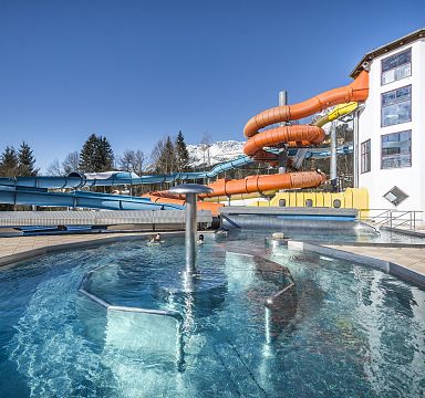 Water park with multiple slides and a pool, set against the scenic mountains of Wilder Kaiser.