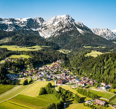 Panoramic view of the Wilder Kaiser mountain range with a picturesque village in the foreground, lush green forests, and clear blue skies.