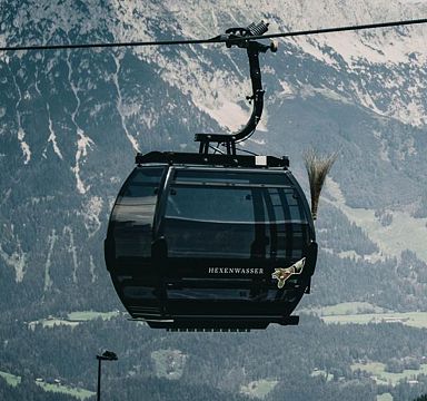 Zwei schwarze Gondeln der SkiWelt-Seilbahn vor alpiner Kulisse, mit schneebedeckten Bergen und grünen Hügeln im Hintergrund, in der Region Wilder Kaiser.