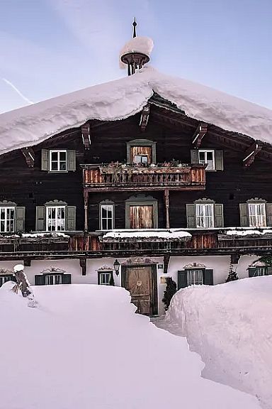 A snow-covered chalet in front of the Wilder Kaiser mountains, with snowy paths and a clear winter sky, representing peaceful austrian Alpine scenery.